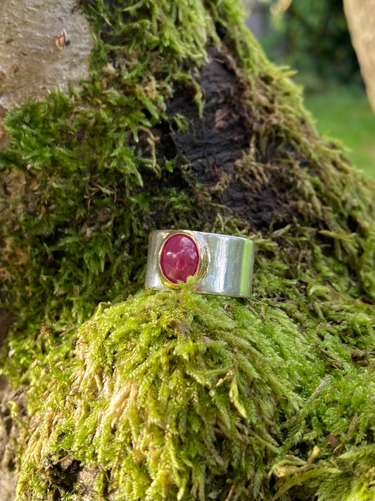  wide silver ring with large oval cabochon red ruby set in yellow gold, resting on moss