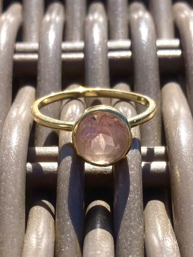 Gold ring with a pink gemstone on a basket weave surface