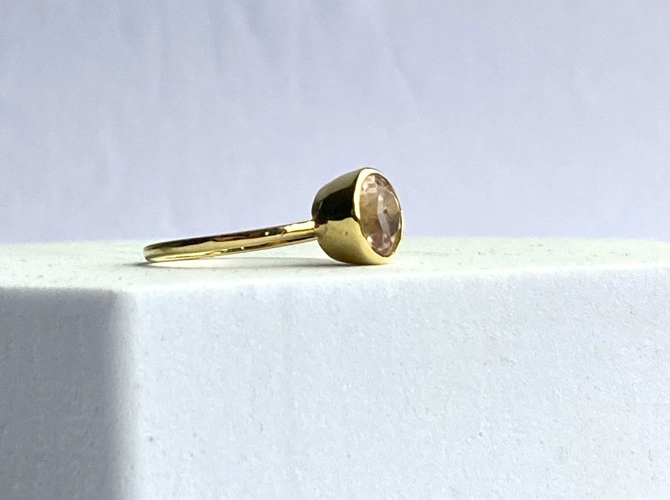 Gold ring with a pink gemstone on a light grey background by Kim Styles Jewellery
