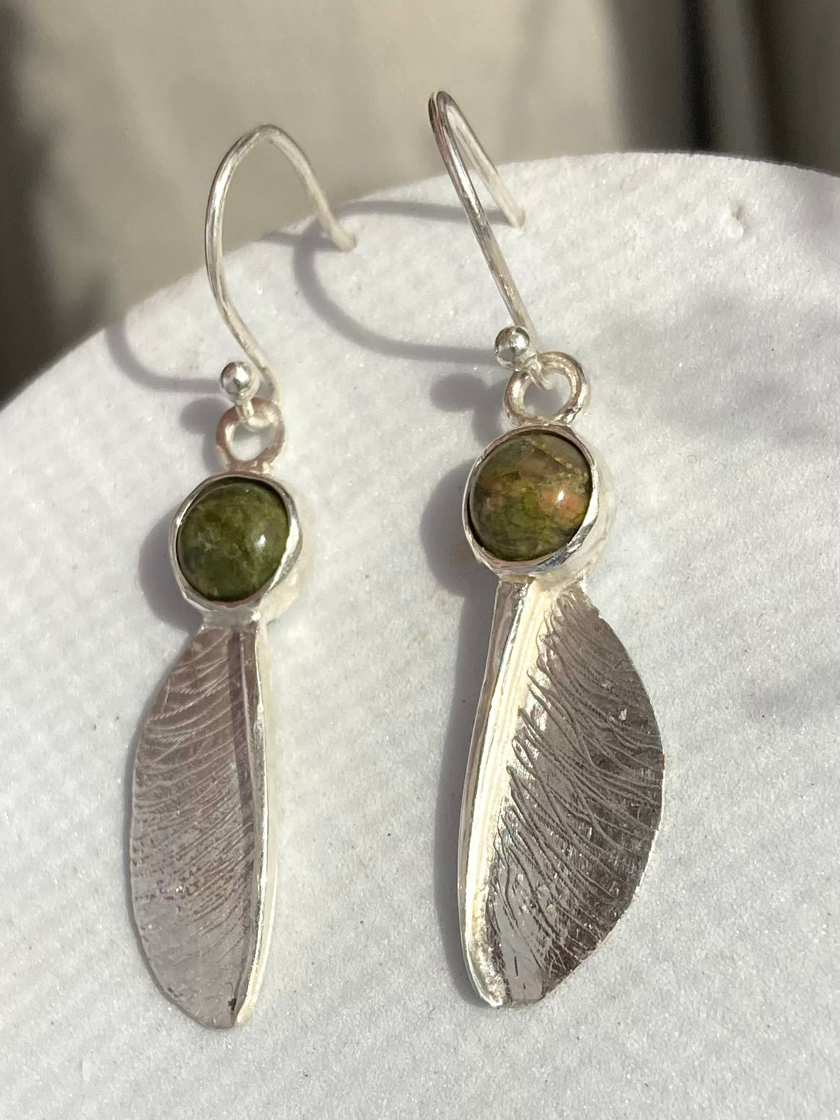 Pair of sterling silver sycamore seed drop earrings by Kim Styles Jewellery set with round cabochon green agates, on grey patterned background