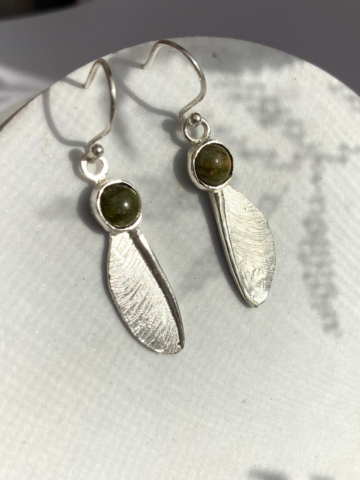 Pair of sycamore seed hook earrings in sterling silver by Kim Styles Jewellery set with round cabochon green agates, on grey patterned background