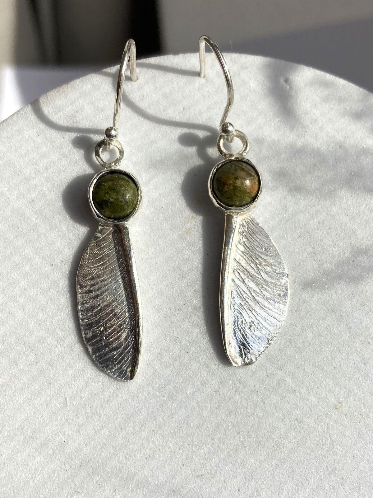 Pair of sycamore seed hook earrings in sterling silver by Kim Styles Jewellery set with round cabochon green agates, on grey background