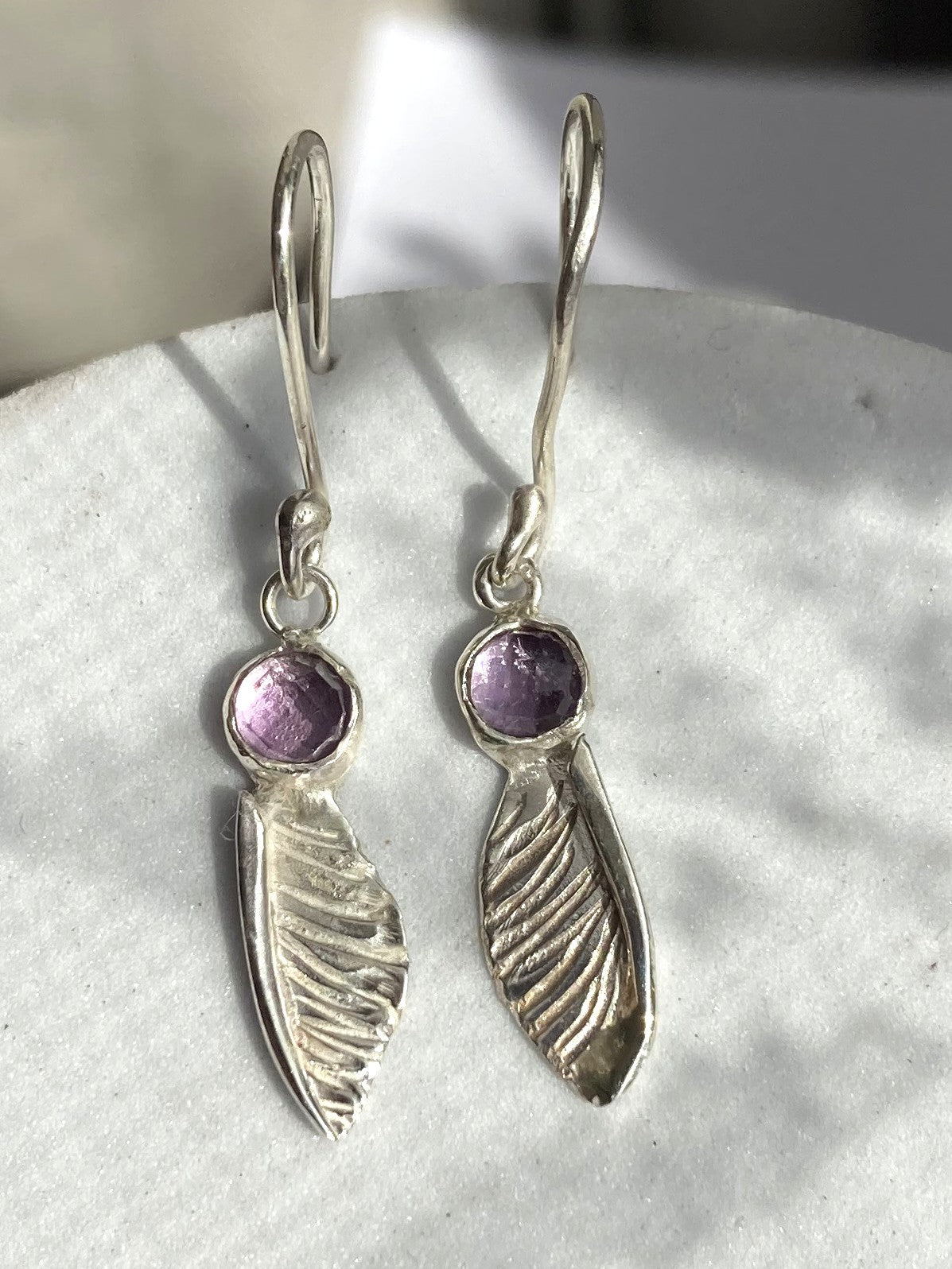 handmade textured silver sycamore seed dangle earrings by Kim Styles Jewellery set with round chequerboard cut amethysts, on patterned grey background
