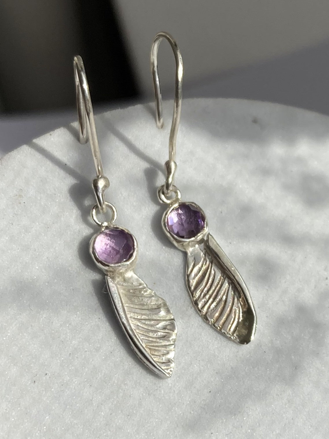 handmade textured  silver sycamore seed hook earrings by Kim Styles Jewellery set with round chequerboard cut amethysts, on patterned grey background