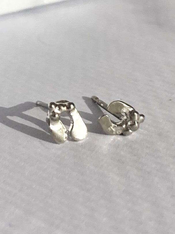 A pair of tiny sterling silver mistletoe leaf stud earrings resting on a light grey surface.