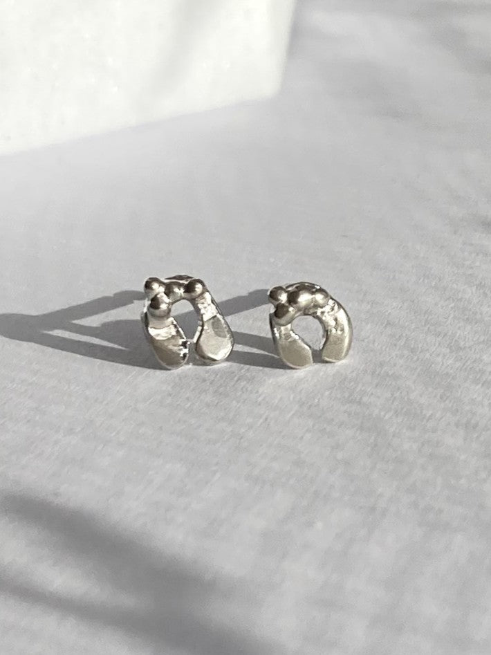 A pair of textured silver mistletoe theme earrings resting on a light grey fabric surface with soft shadows.