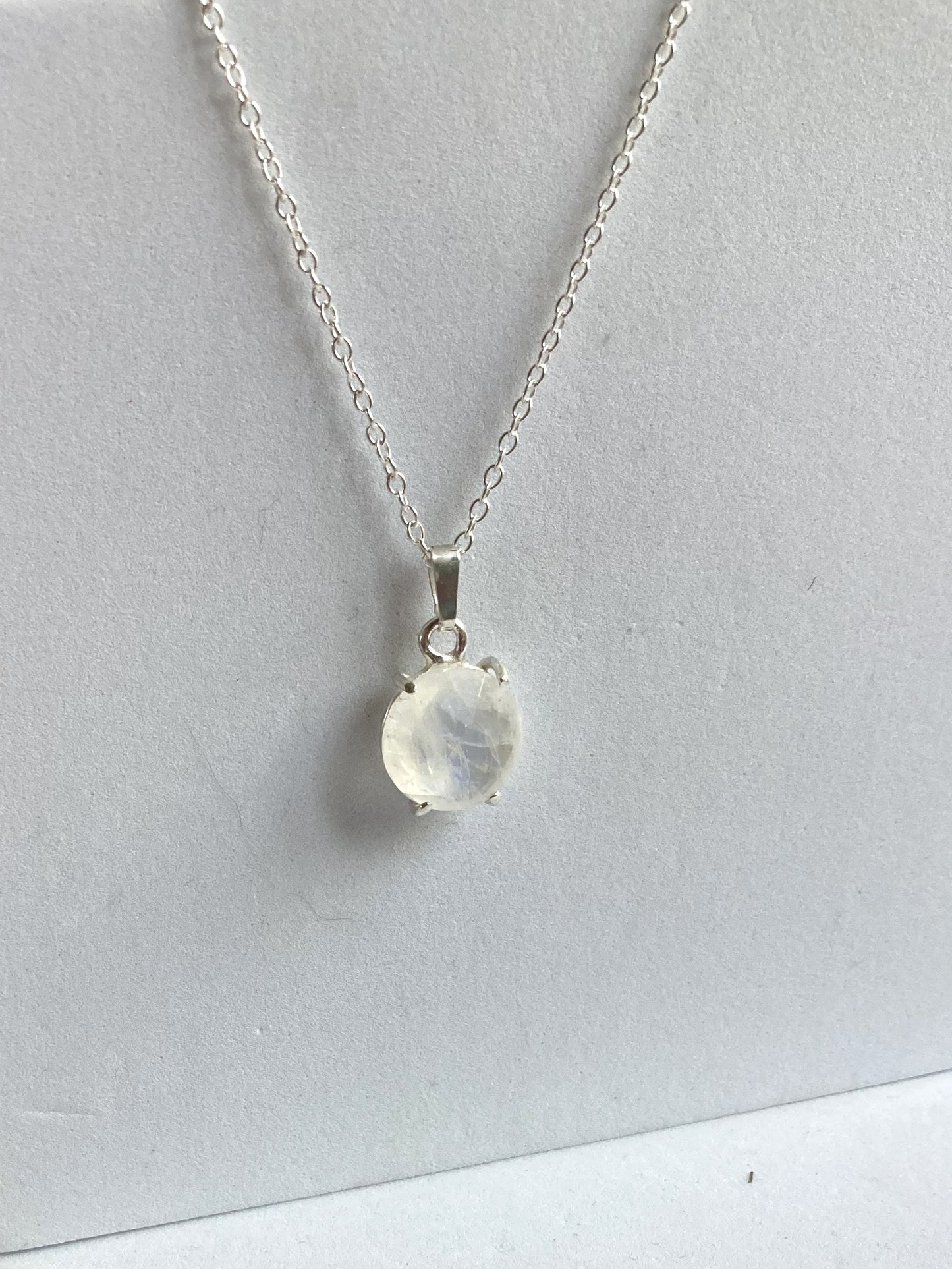 Silver necklace with a round moonstone pendant on a light grey background