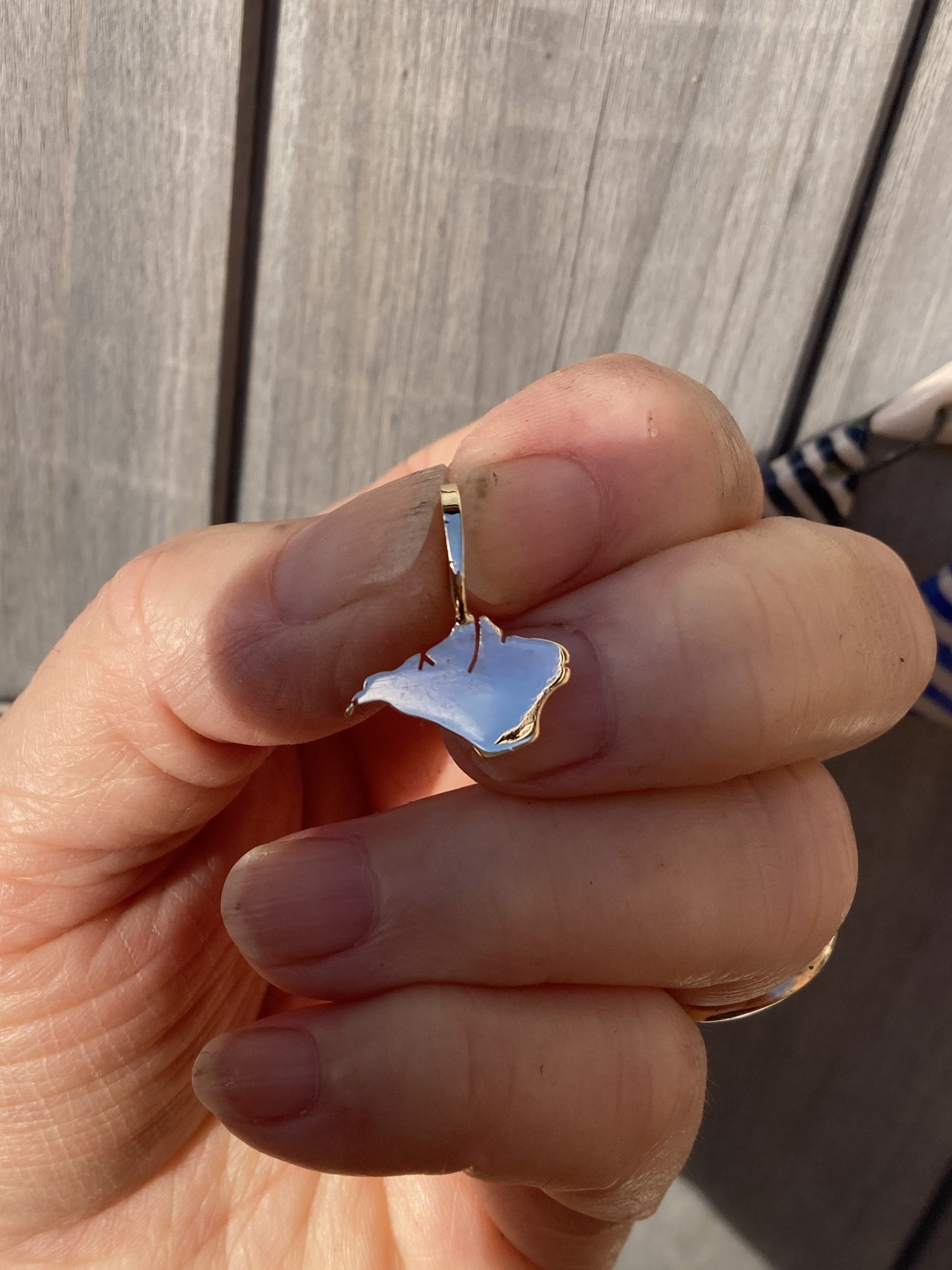Hand holding a gold silhouette pendant of the Isle of Wight against a wooden background