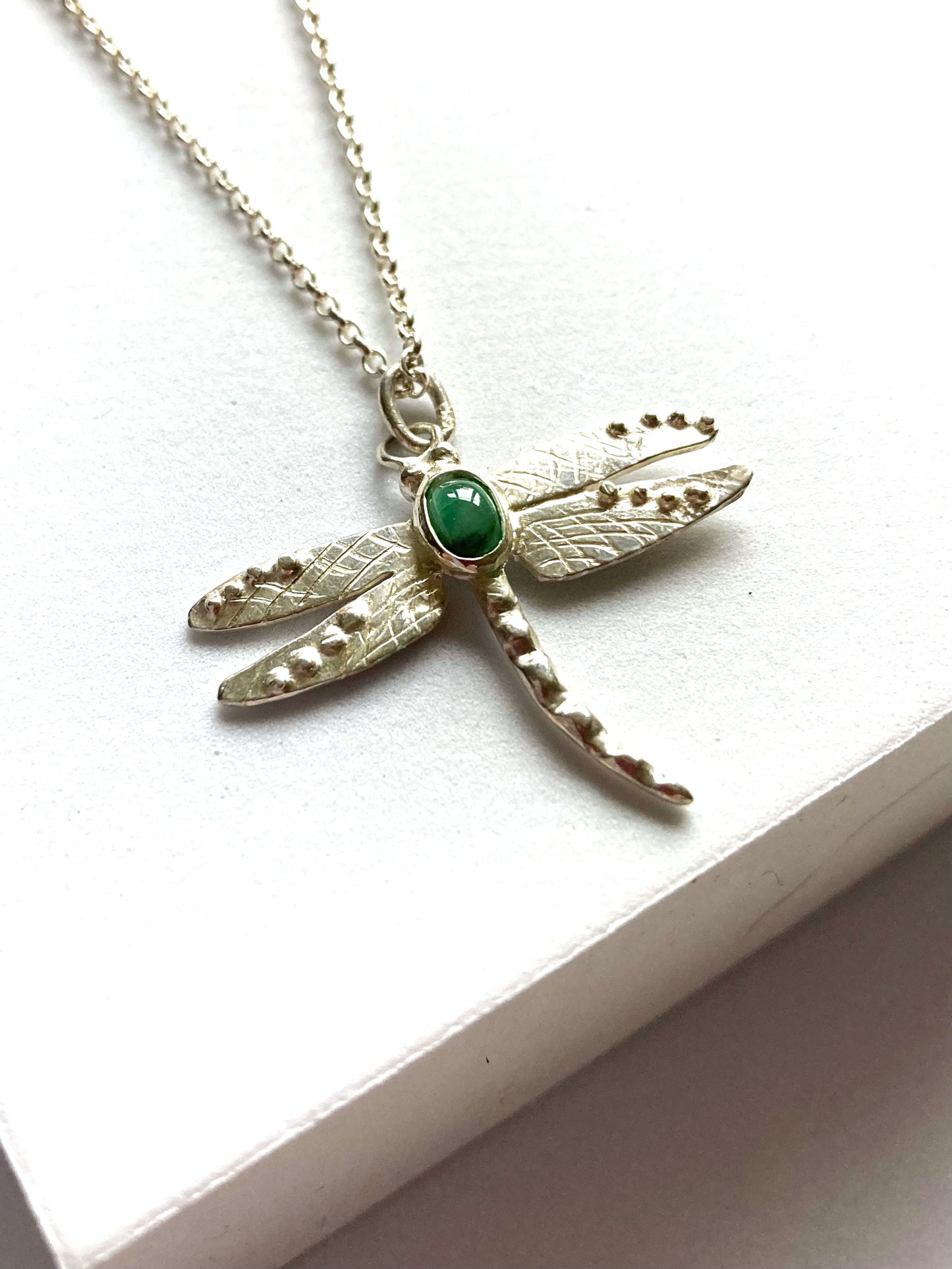 Silver dragonfly pendant with a green emerald gemstone on a white background