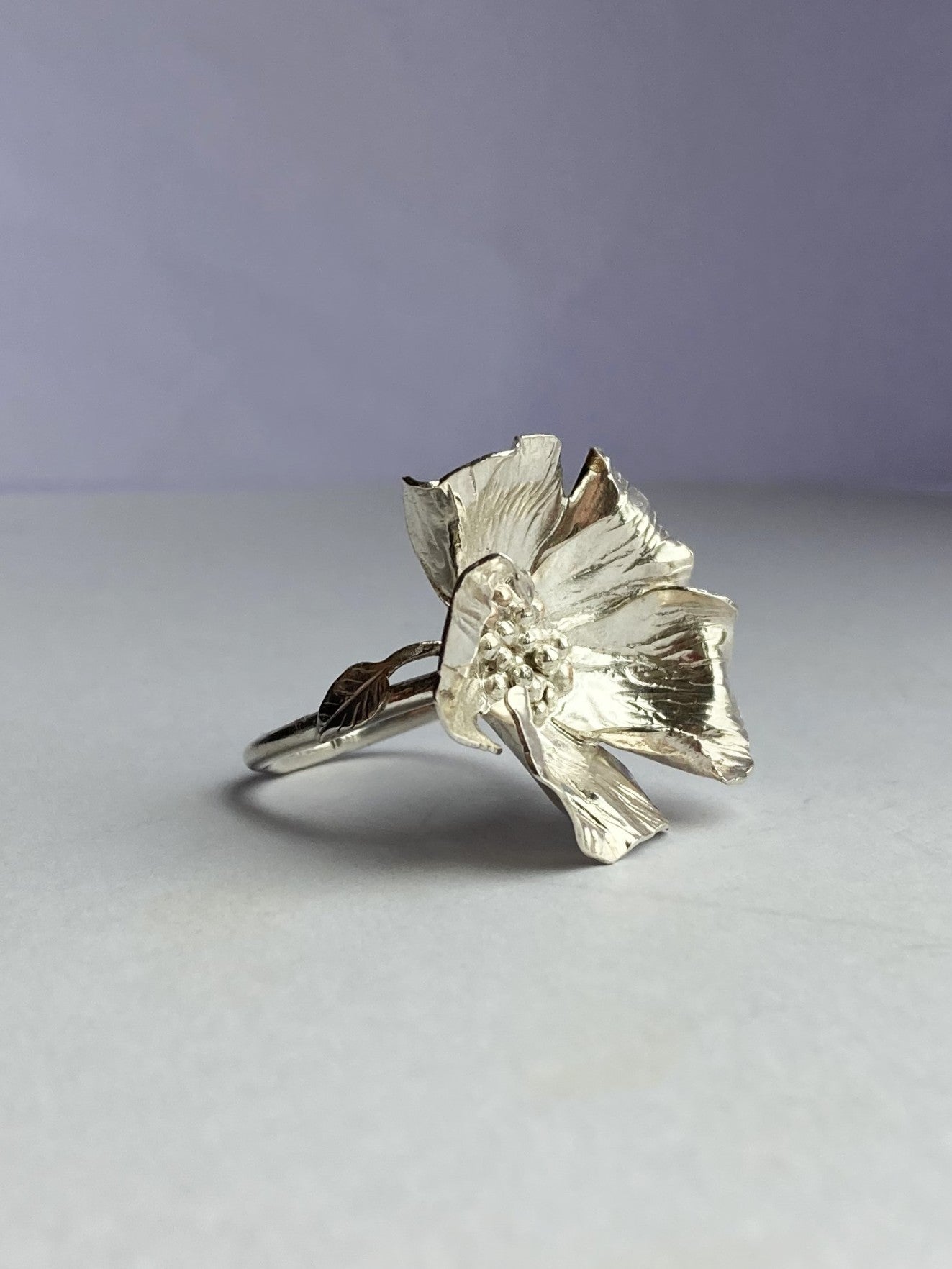 Hand forged poppy ring with leaf detail, by Kim Styles Jewellery, on grey background
