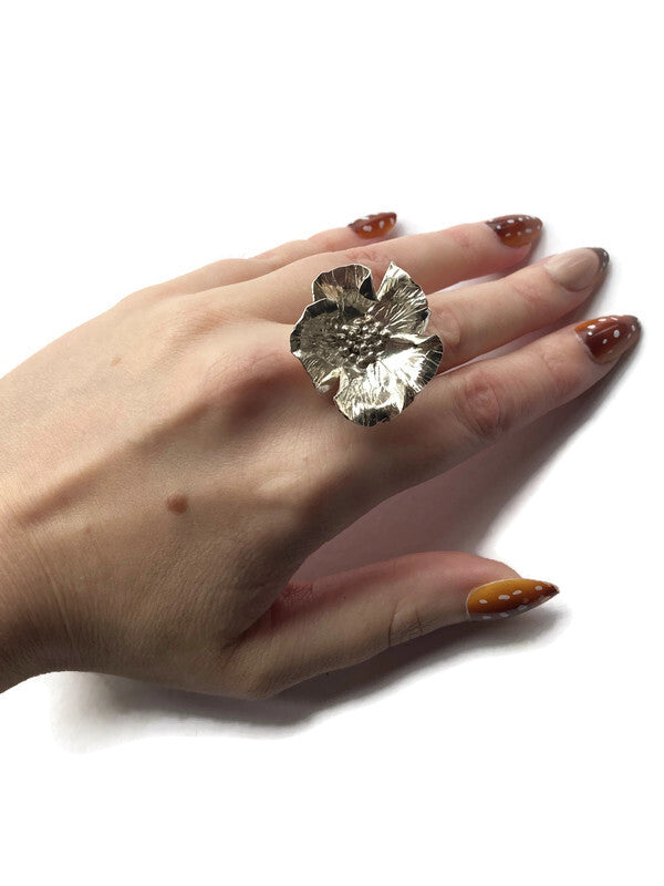 large hand forged floral poppy ring on hand with brown nails, on white background