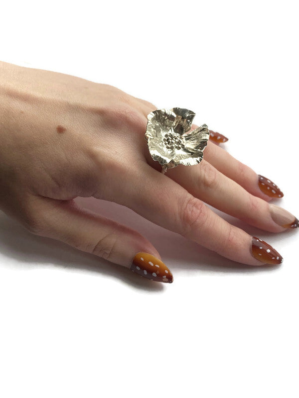 large floral statement ring worn on hand with brown and white spotty nails, on white background
