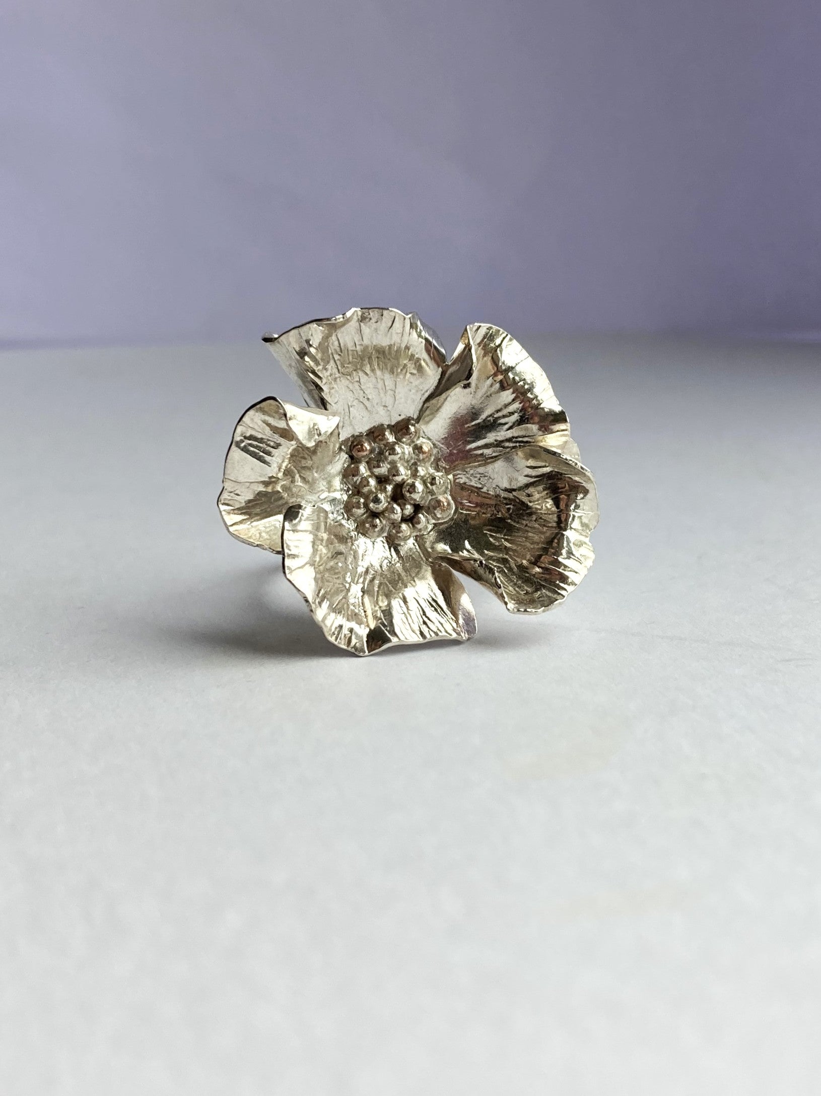 silver wrinkled poppy floral ring on grey background
