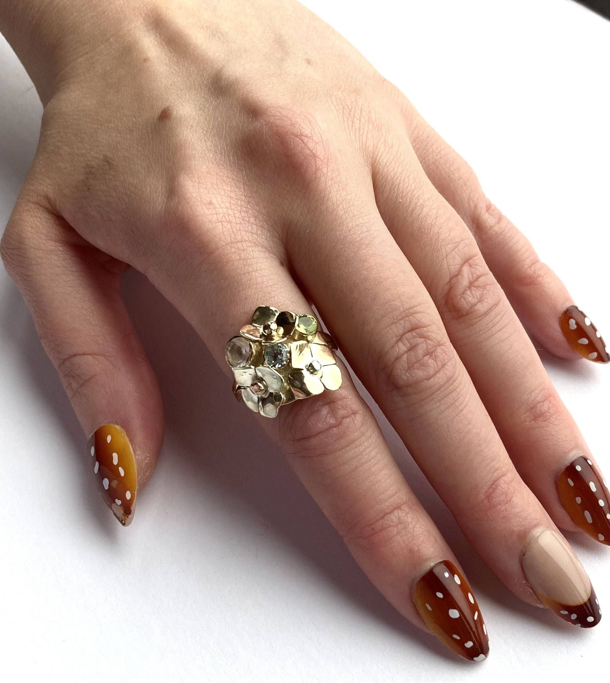 Hand wearing a decorative floral gold ring with brown nail polish on a white background