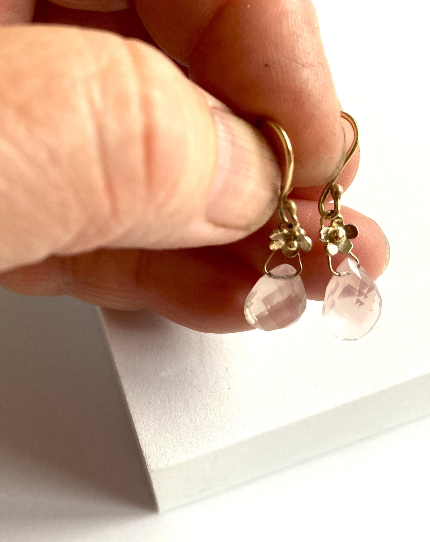 Gold earrings with pink gemstones held by a hand against a white background