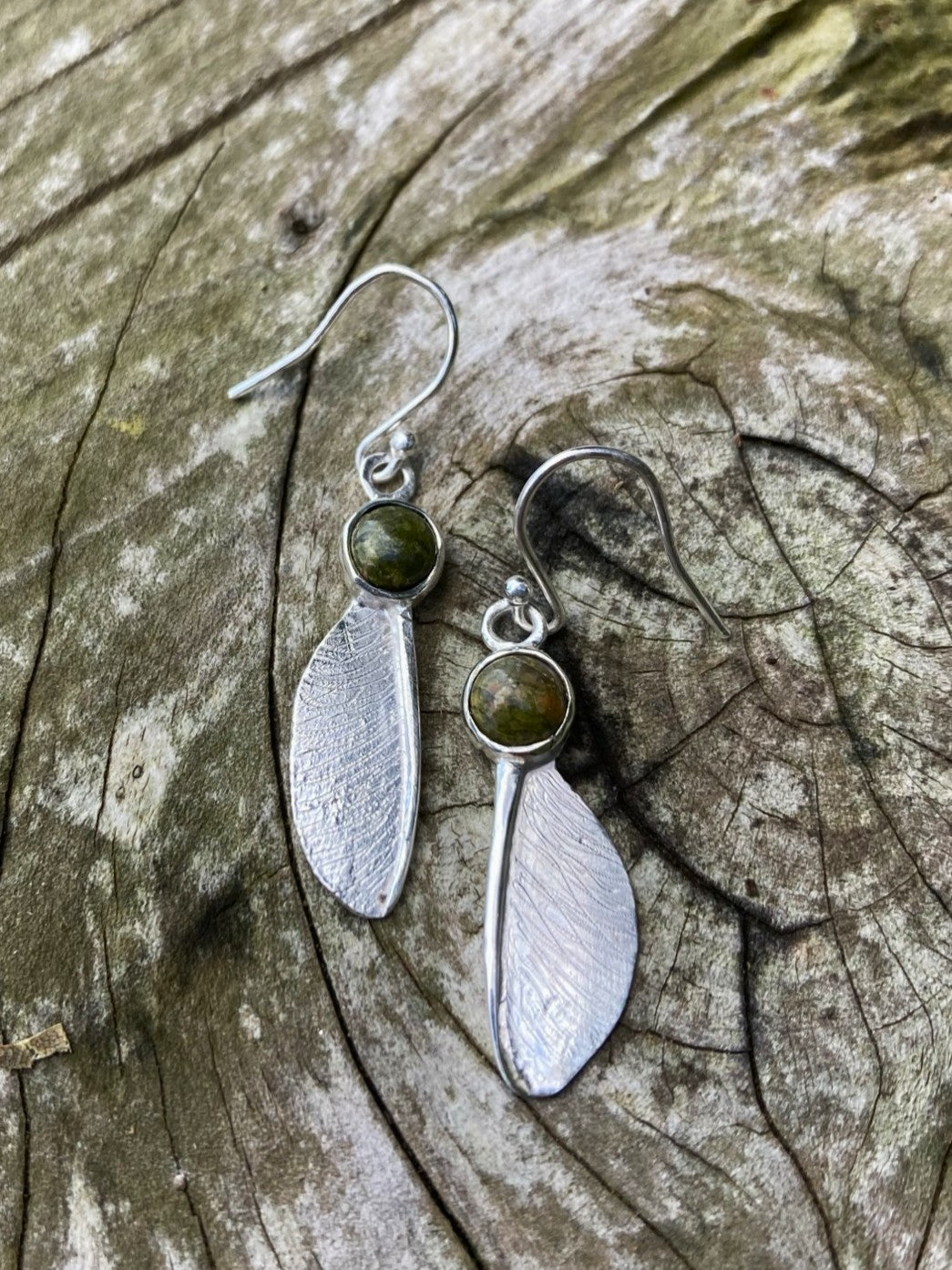 Pair of hook earrings in sterling silver  with sycamore seed design set with round cabochon green agates, on textured wood background