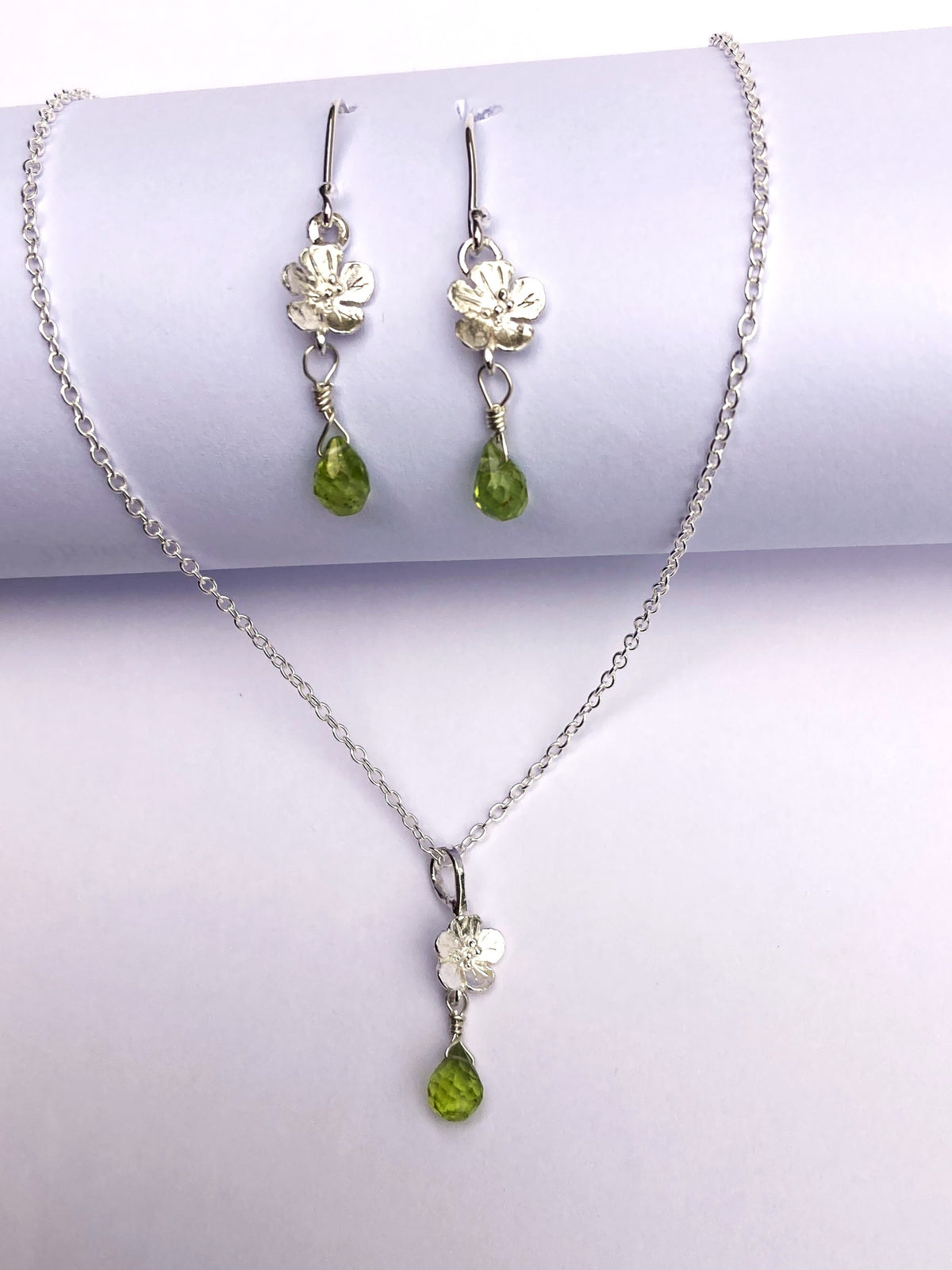 Sterling Silver necklace and drop earring set with green teardrop peridot gemstones and silver flower charms, displayed on a white background.