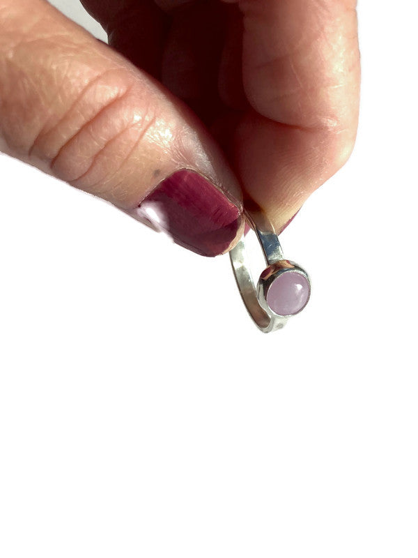 Hand holding a silver ring with a pink stone against a white background