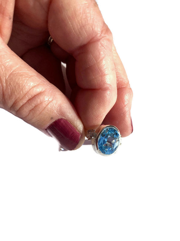 Hand holding a silver ring with a blue gemstone against a white background