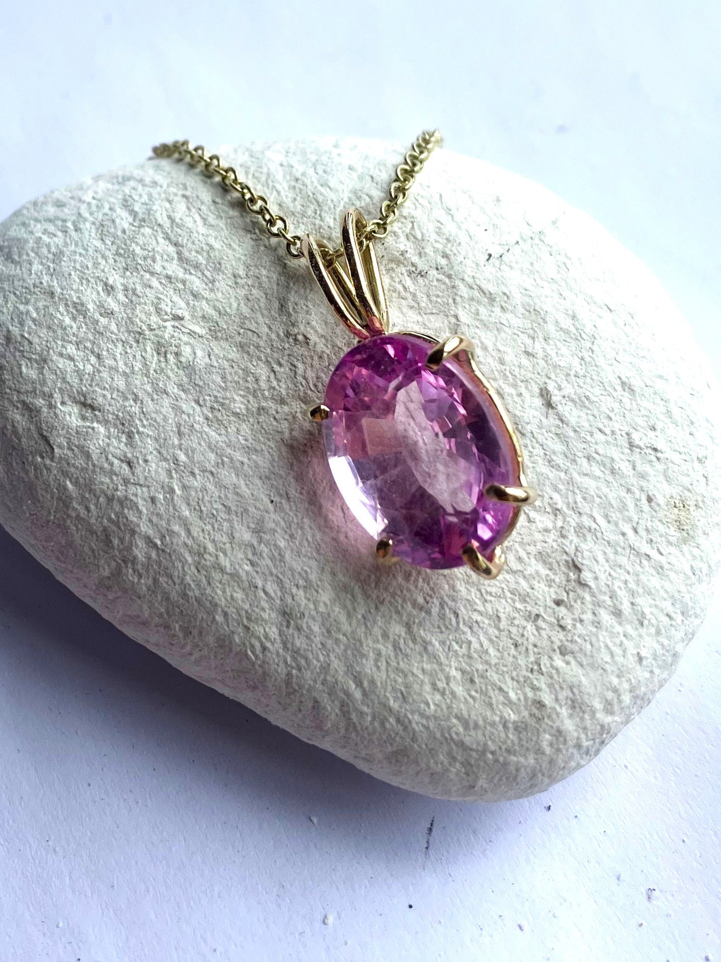luxury 11ct  rich pink spinel oval pendant set in gold prong setting on gold chain,  hand made by Kim Styles, on white pebble background