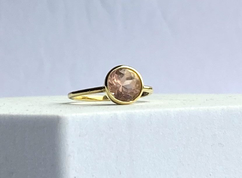 Gold ring with a pink gemstone on a light gray background