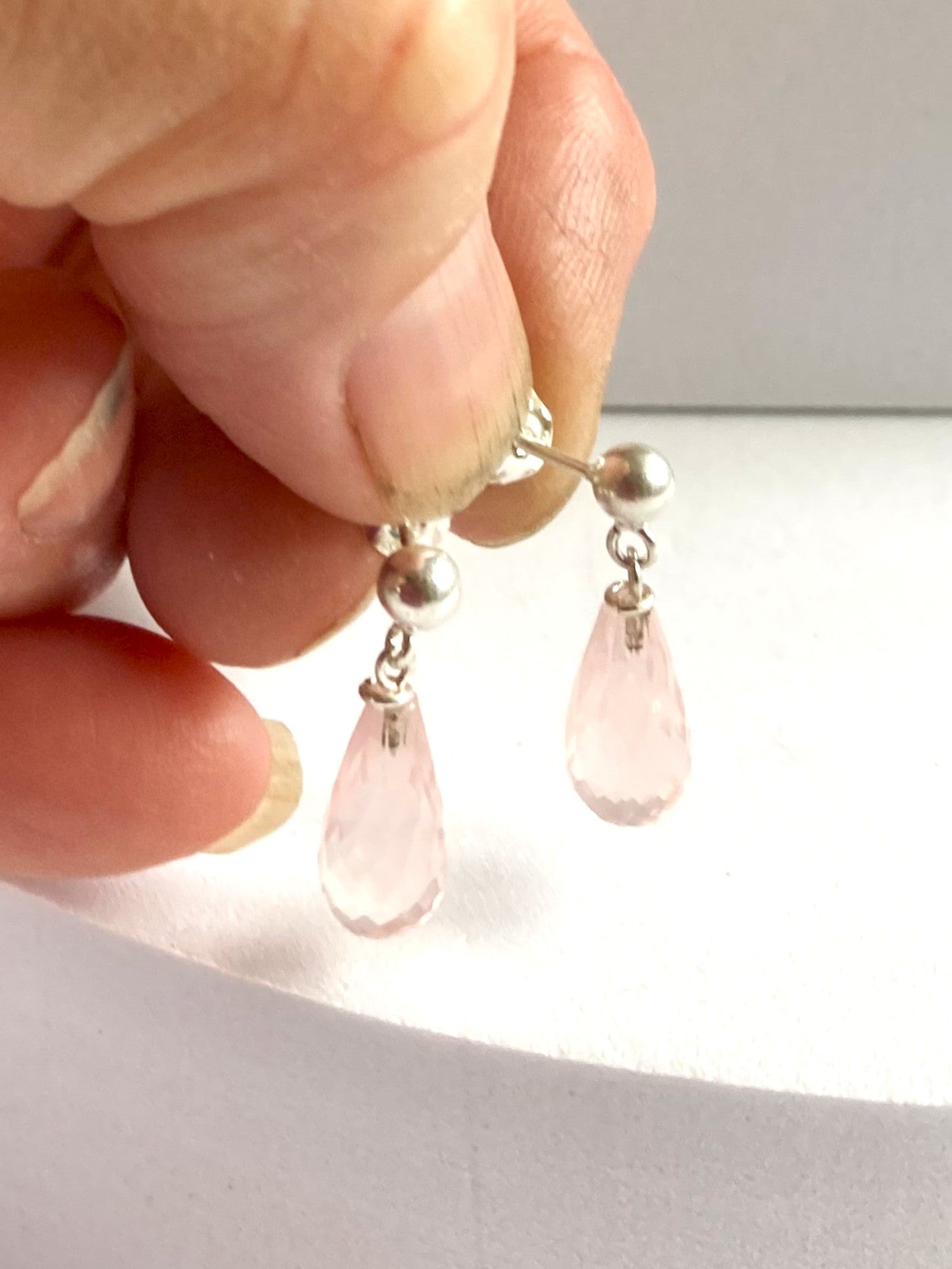 Rose quartz teardrop earrings with silver hooks held between fingers against a neutral background