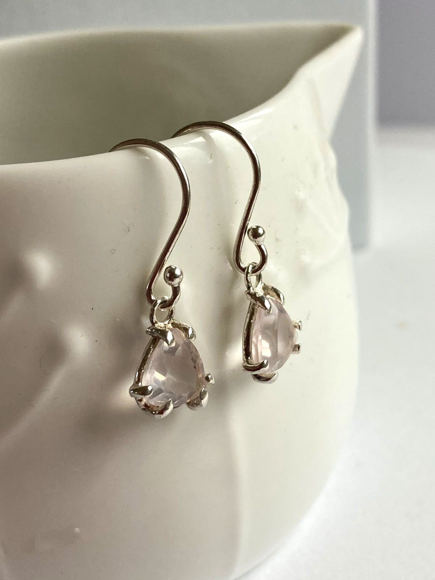 Trillion shaped pink rose quartz earrings on a white ceramic dish