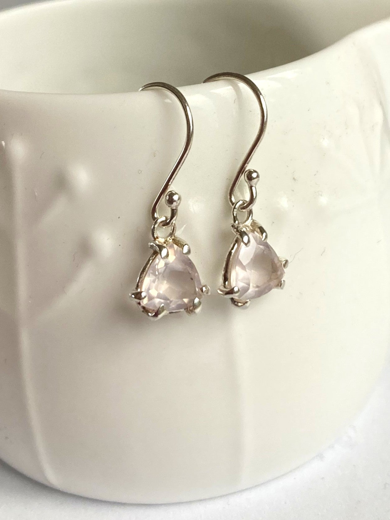 Silver earrings with pink gemstones on a white ceramic surface