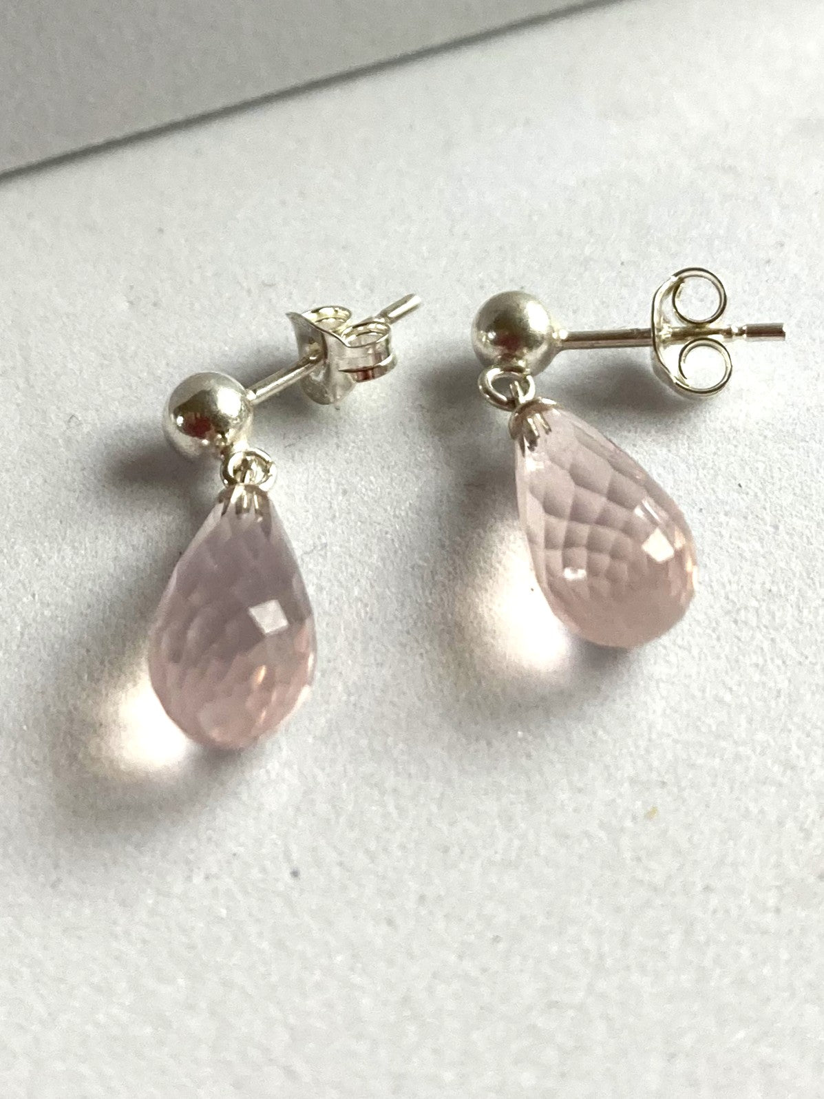 Pair of silver earrings with pink teardrop-shaped stones on a light gray background
