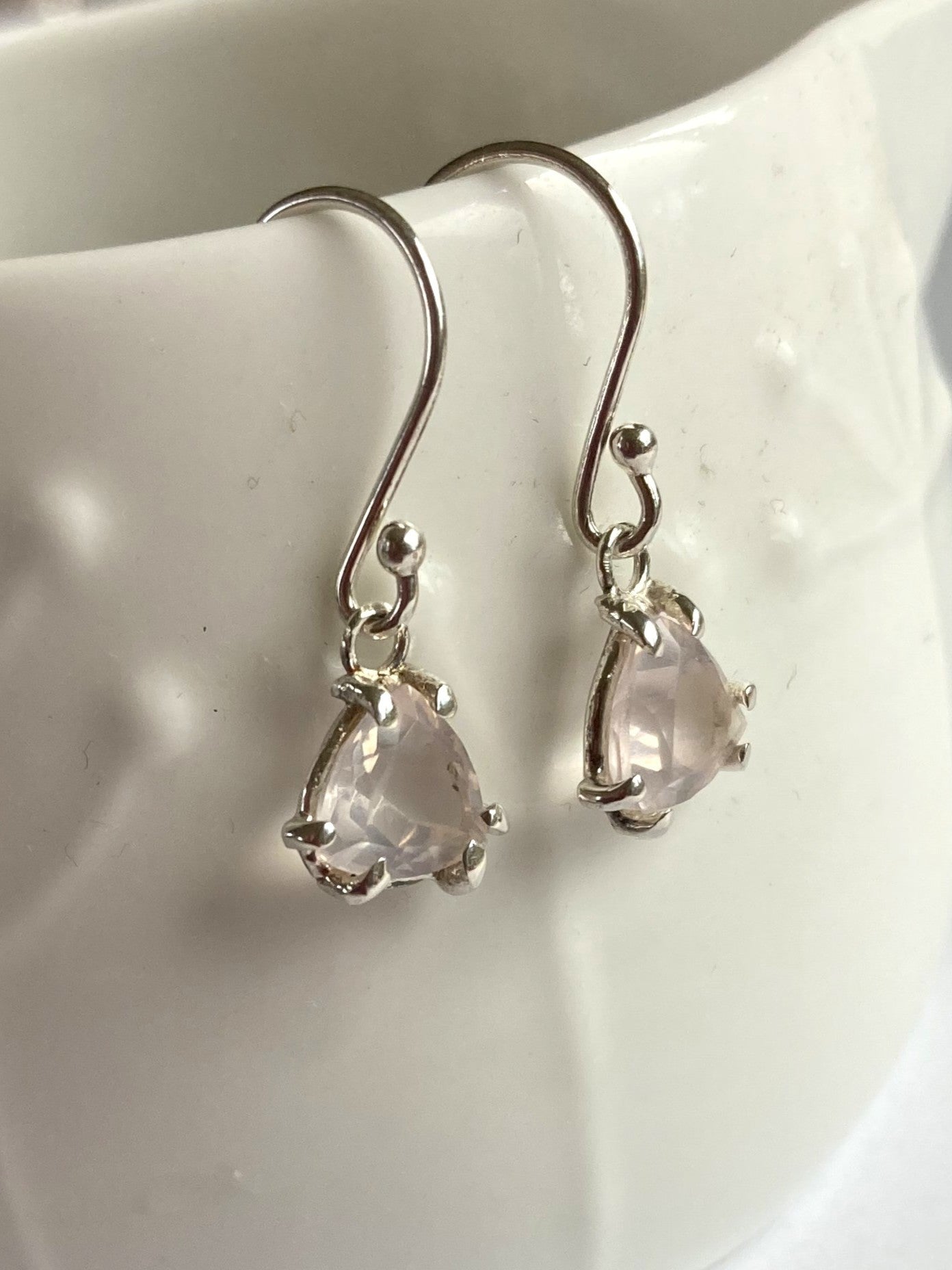 Silver earrings with trillion-shaped pink gemstones on a white ceramic surface