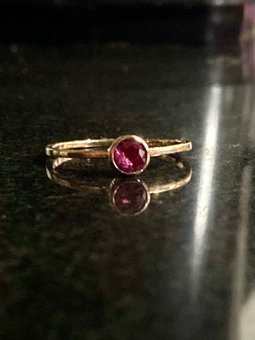 Gold single stone ring with a red ruby gemstone by Kim Styles jewellery on a reflective black surface