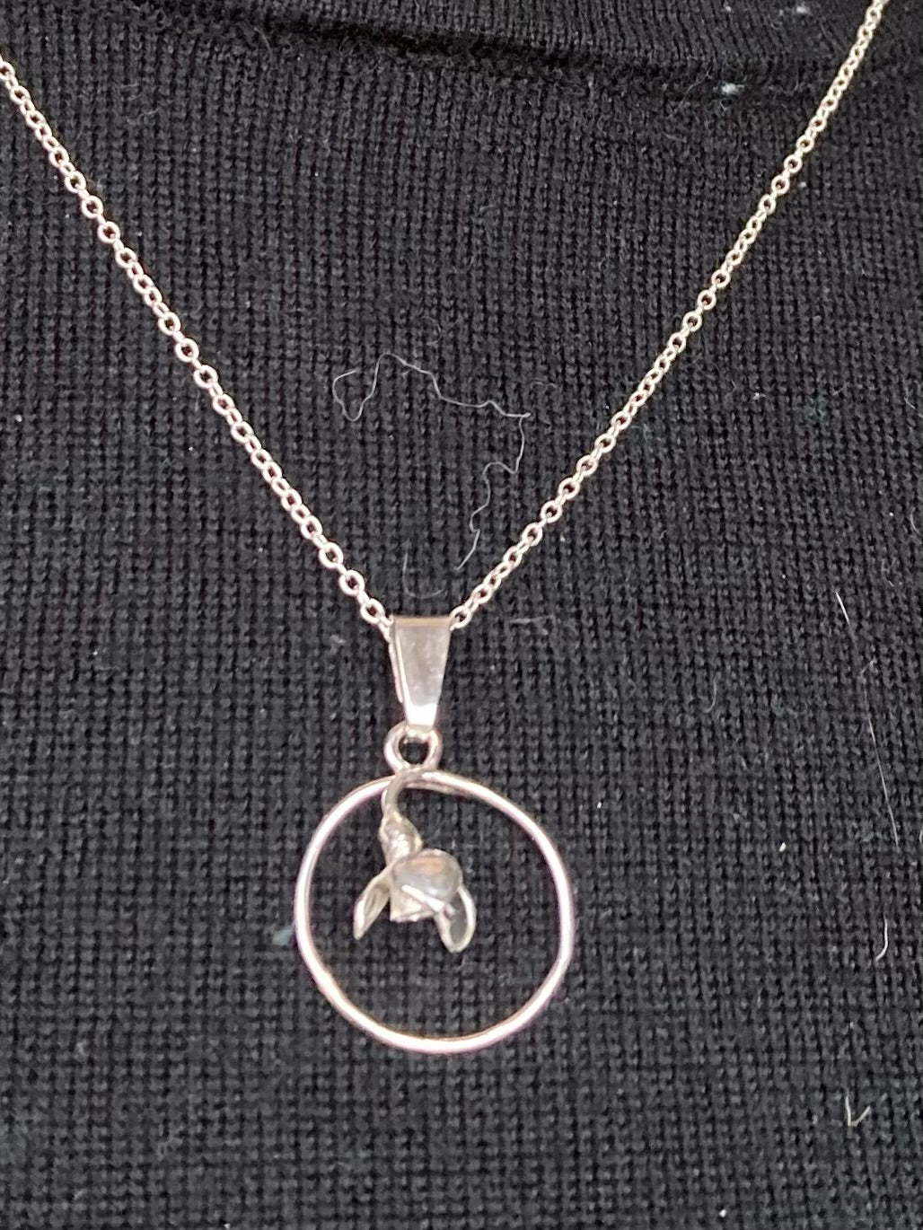 Silver circle pendant with flower inside on black background