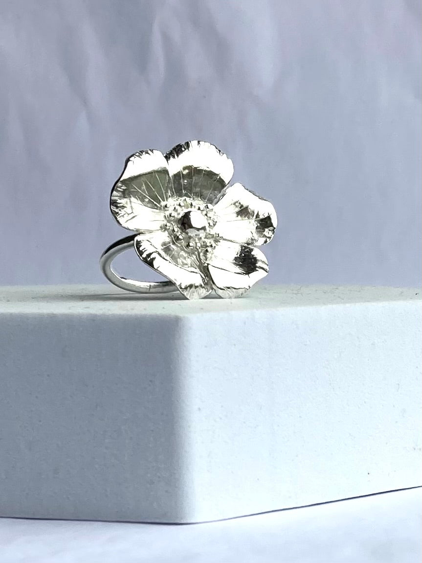Silver cocktail ring with a floral design on a light grey background