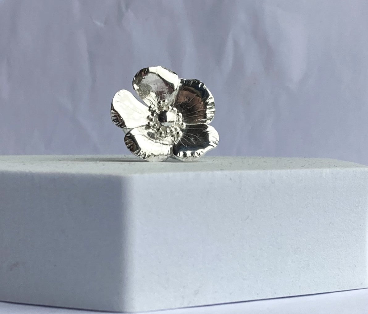 Silver flower cocktail ring on a grey surface with a grey background