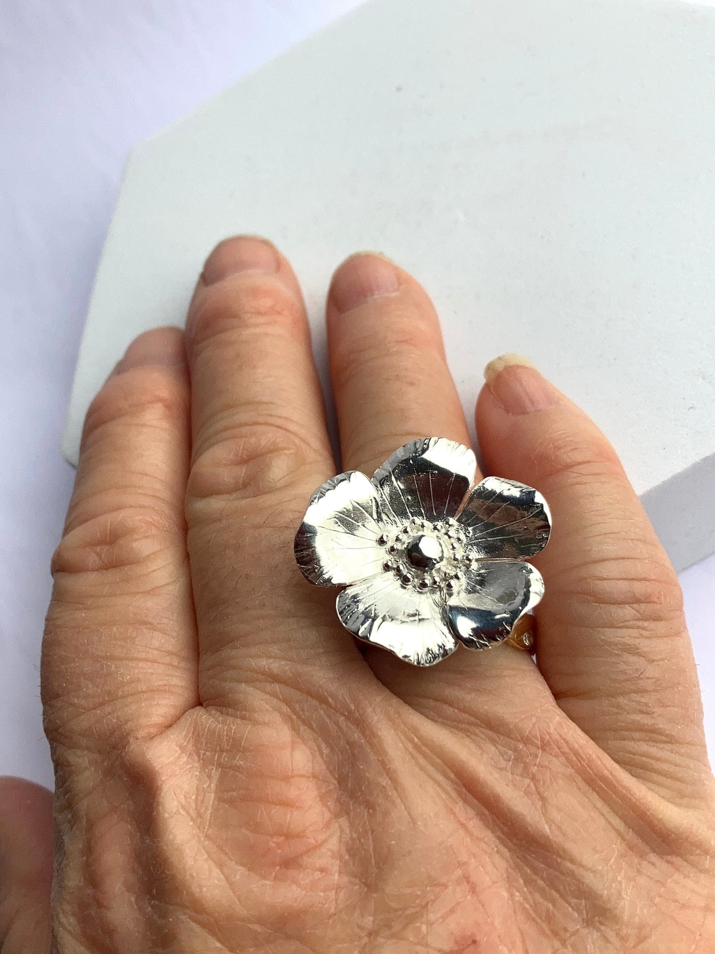 Silver flower-shaped cocktail ring by Kim Styles Jewellery on a hand against a white background