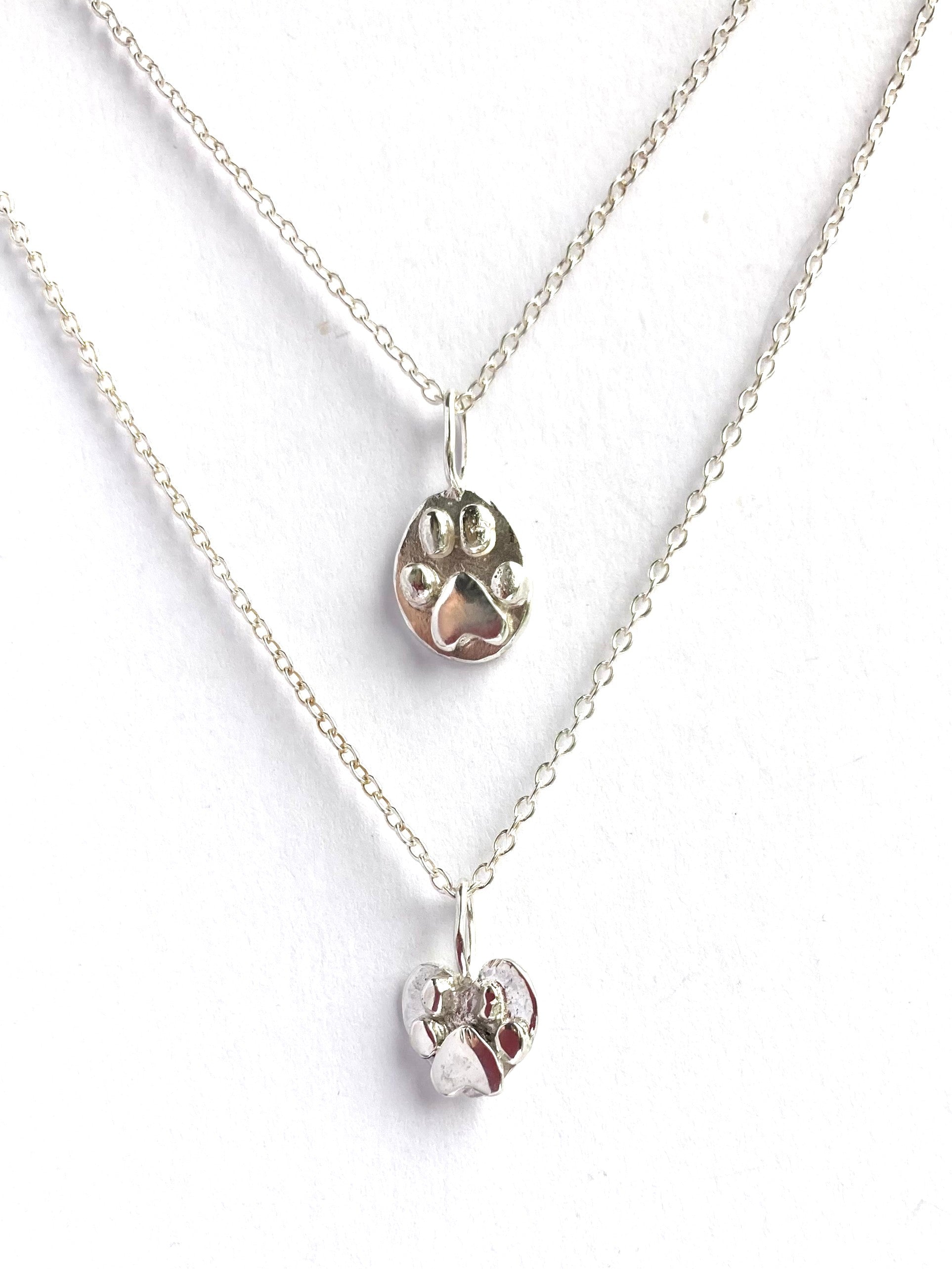 two silver paw print pendants on white background