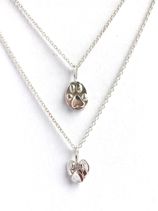 two silver paw print pendants on white background