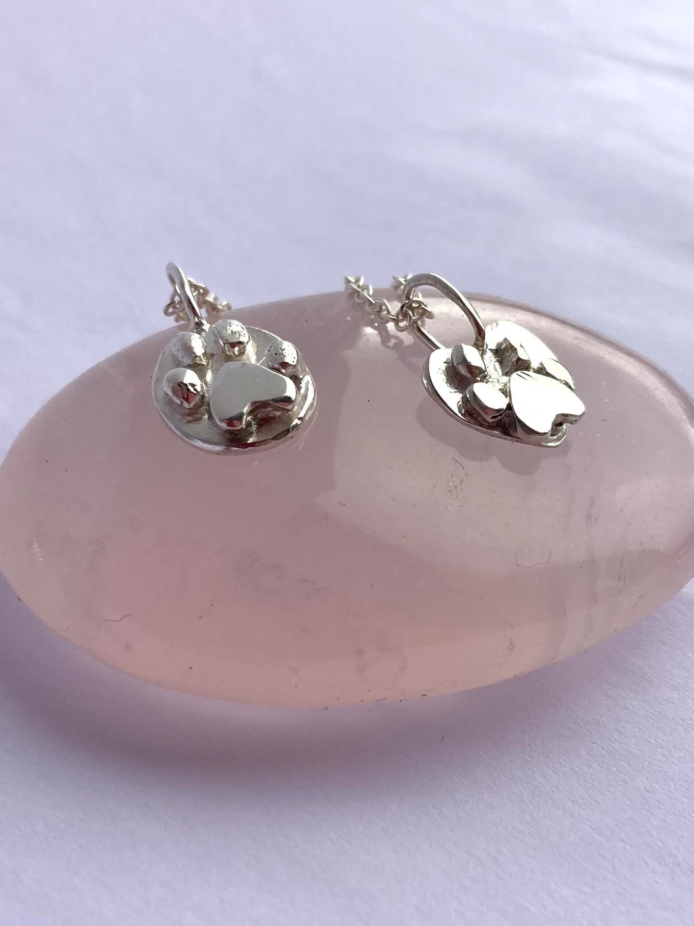 two 3 dimensional pawprint sterling silver pendants by Kim Styles Jewellery, on rose quartz pebble