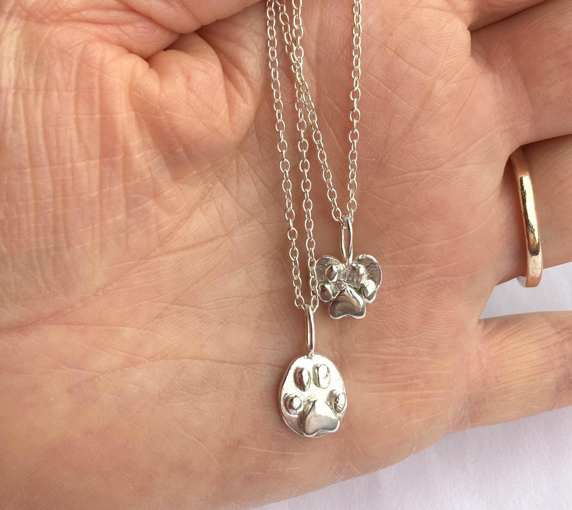 two silver 3D paw print pendants on hand