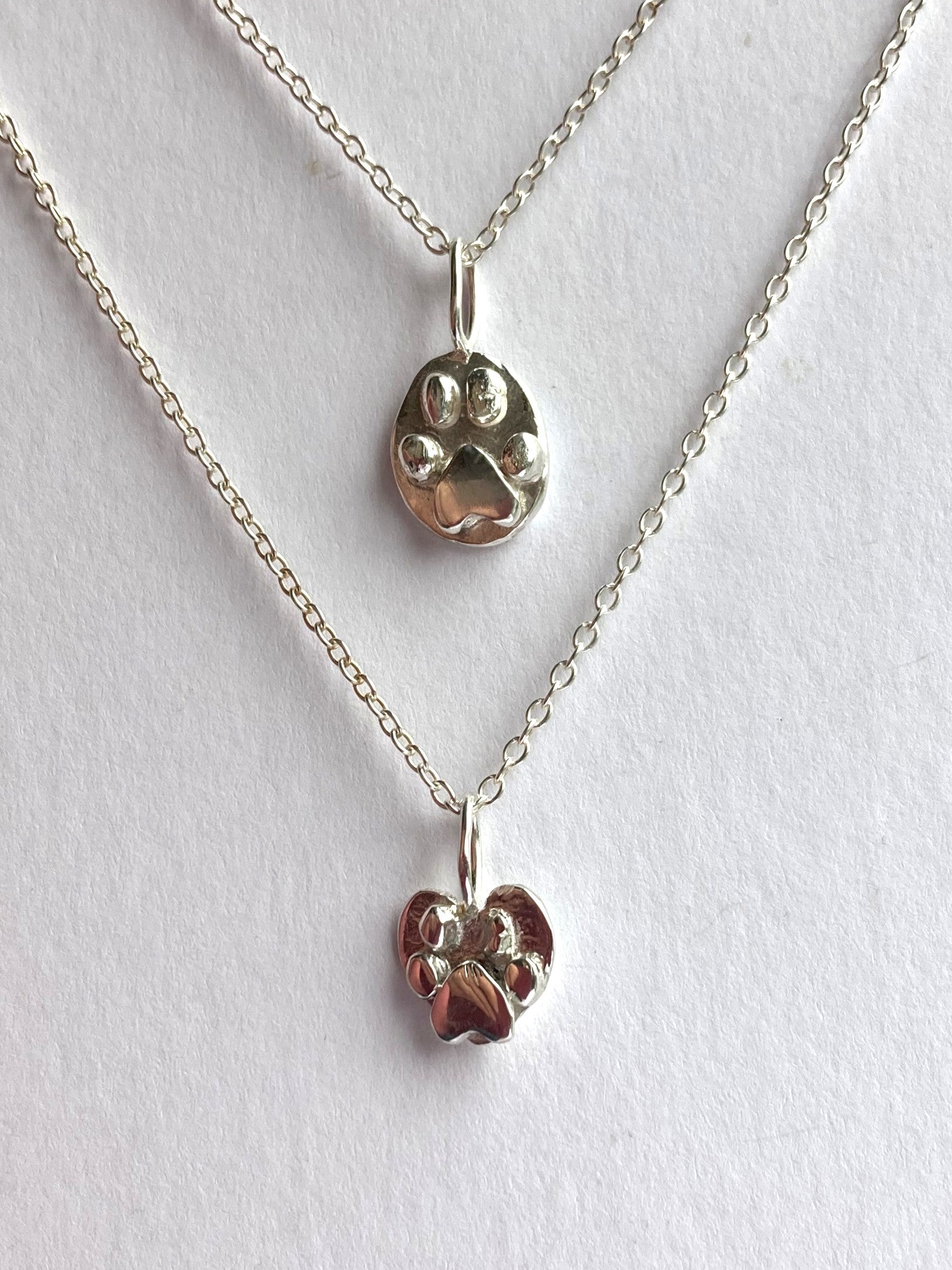 two sterling silver chunky pawprint pendants on chains, on white background