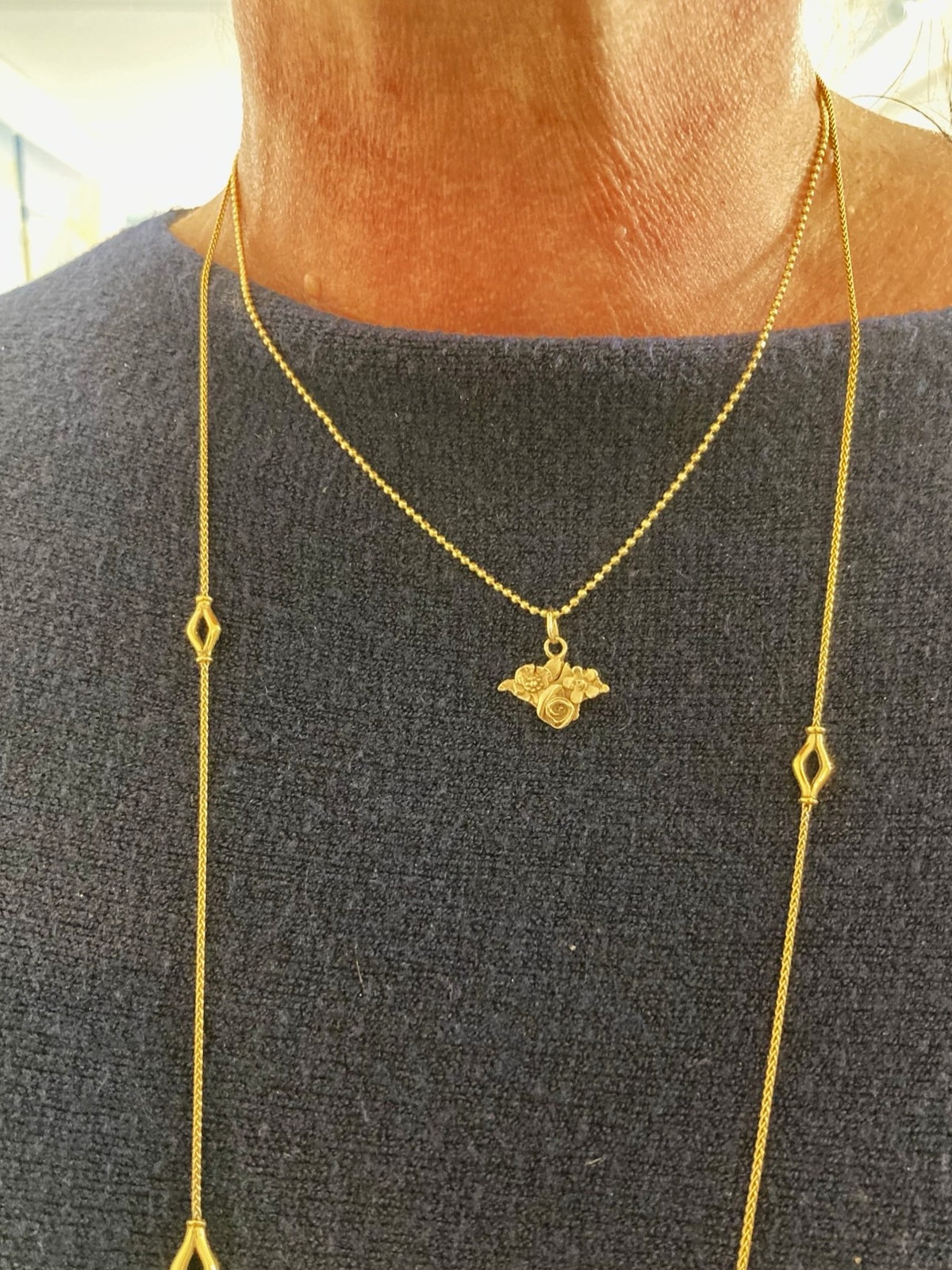 A close-up of a person's neck and chest wearing a gold Isle of Wight silhouette necklace with a small floral and leaf pattern, by Kim Styles Jewellery 