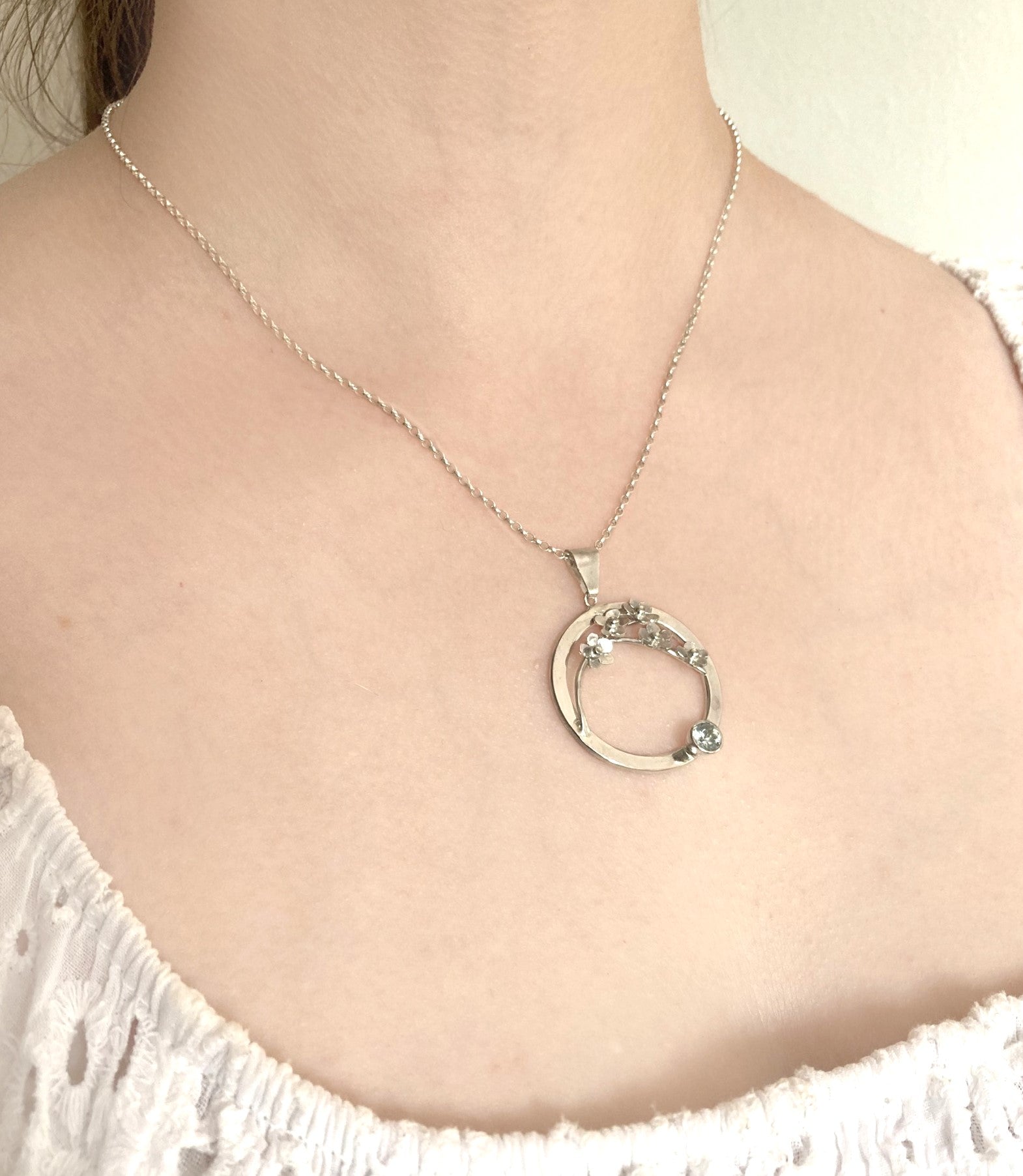 woman's neck wearing silver chain and floral circle pendant