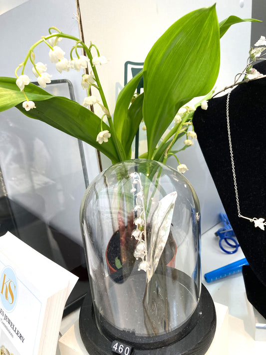 lily of the valley sculpture in glass dome with real lily of the valley flower behind