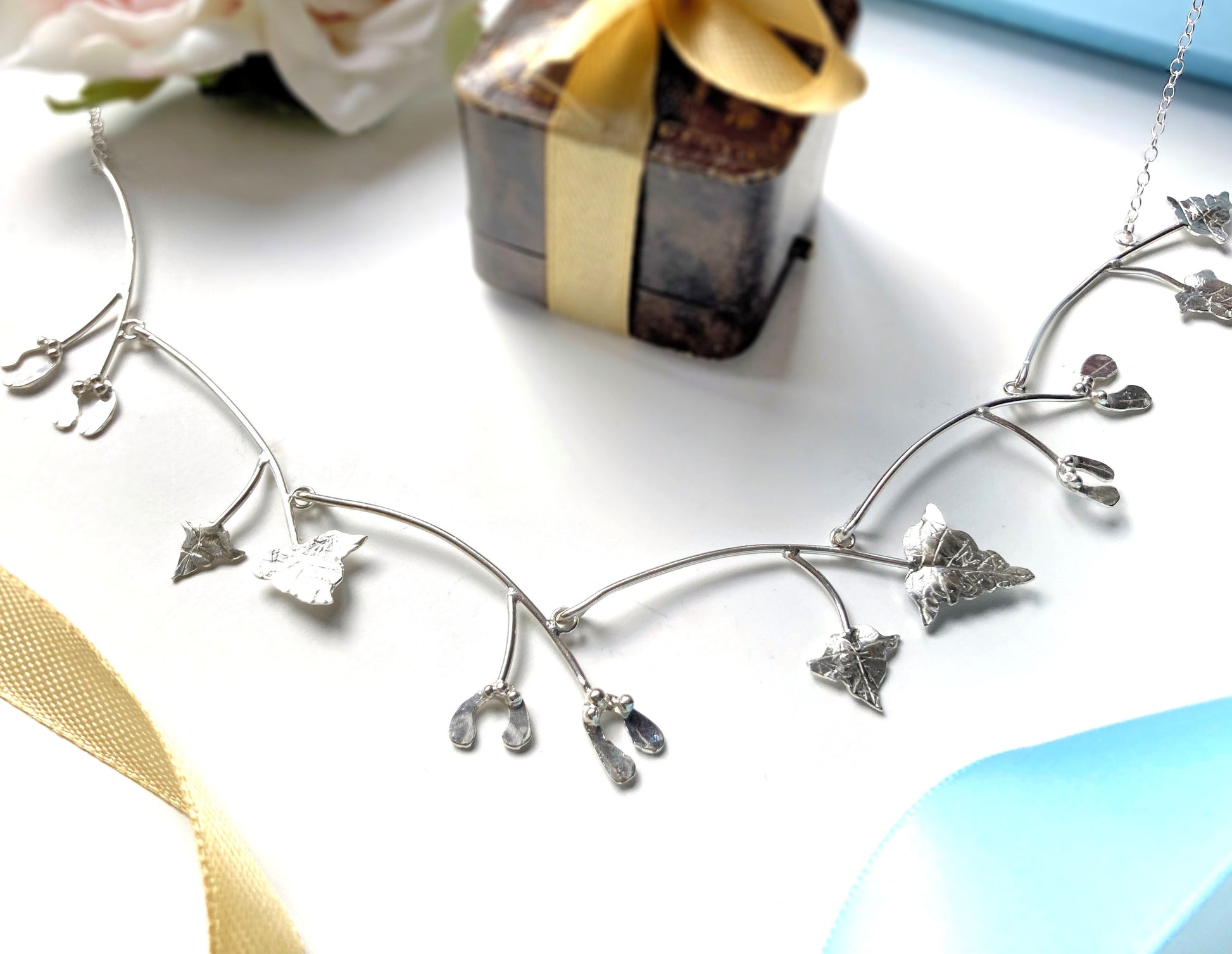 Silver necklace of tiny mistletoe and vine leaves, with a Christmas them background