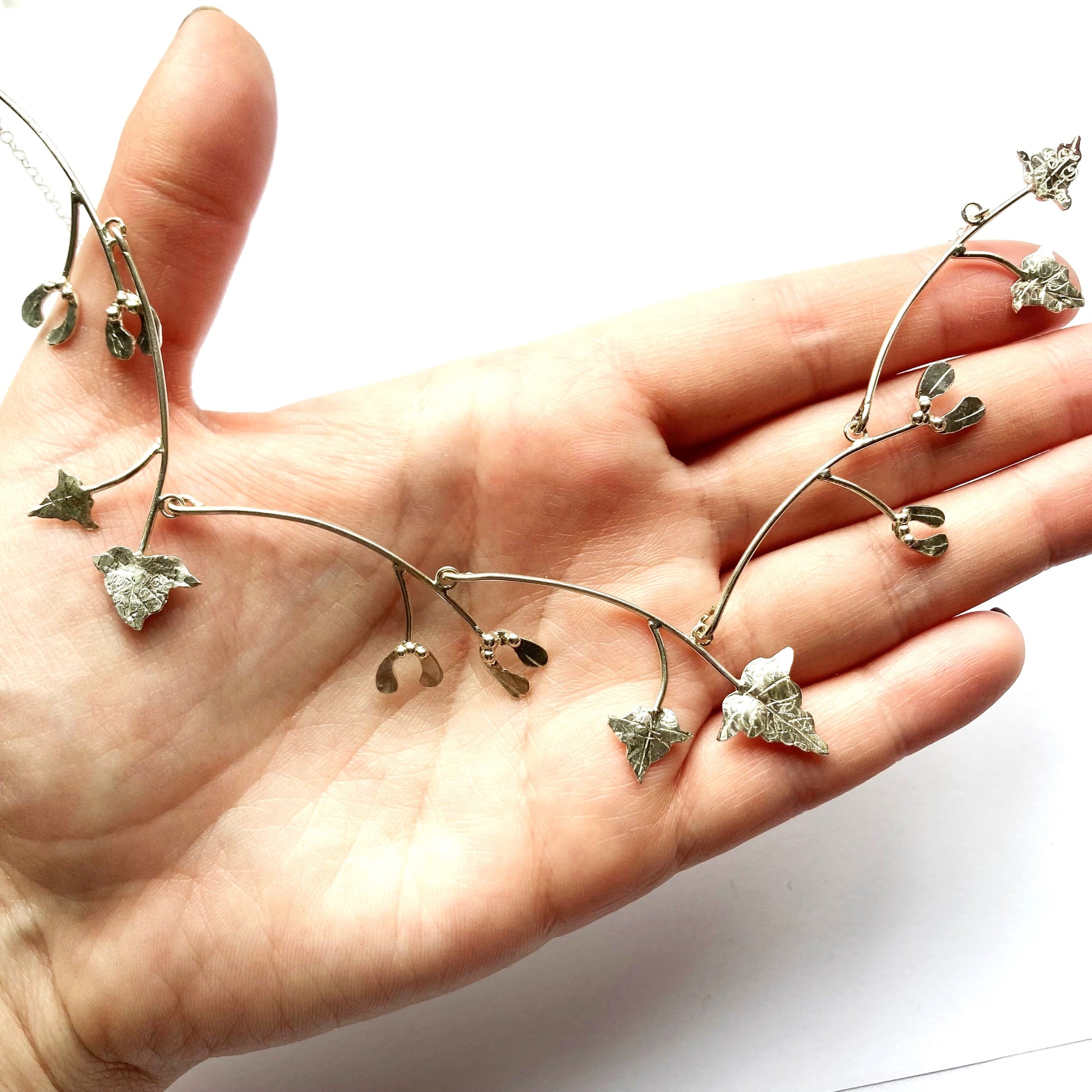 hand holding dainty necklace of silver mistletoe and vine leaves