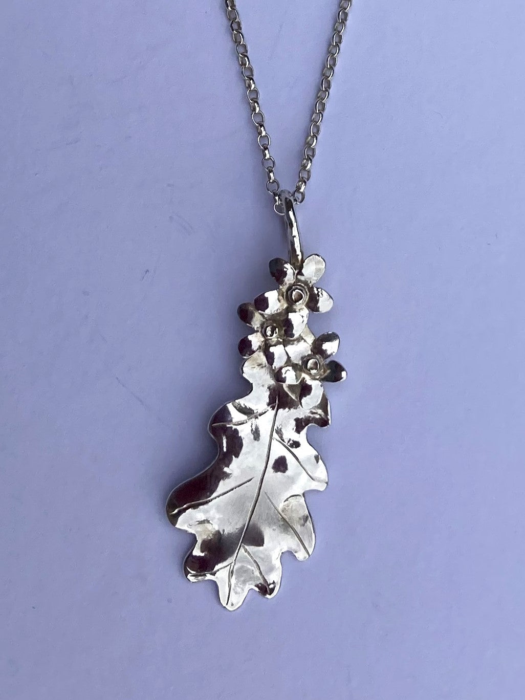 floral pendant in silver with oak leaf and three flowers, on grey background