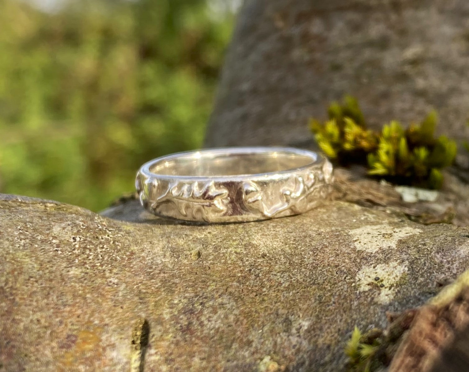 wide ring with oak leaves and acorns in relief around the band, resting on tree bark