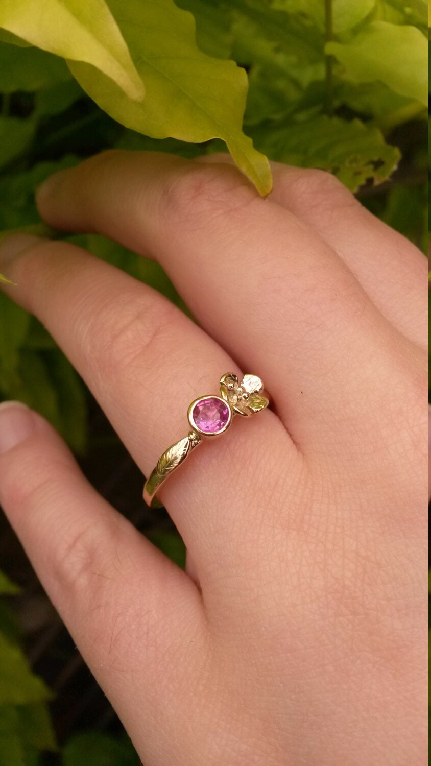 hand wearing gold floral engagement ring with pink gemstone by Kim Styles Jewellery, on leaf background