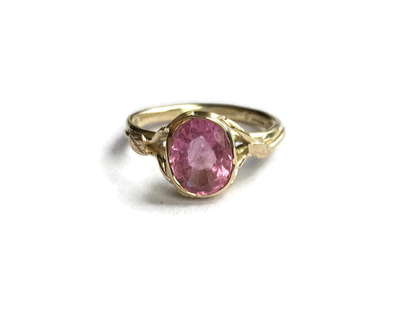 pink oval gemstone in gold ring on white background