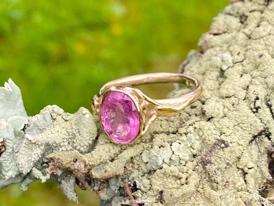 bright pink oval gemstone gold ring resting on lichen